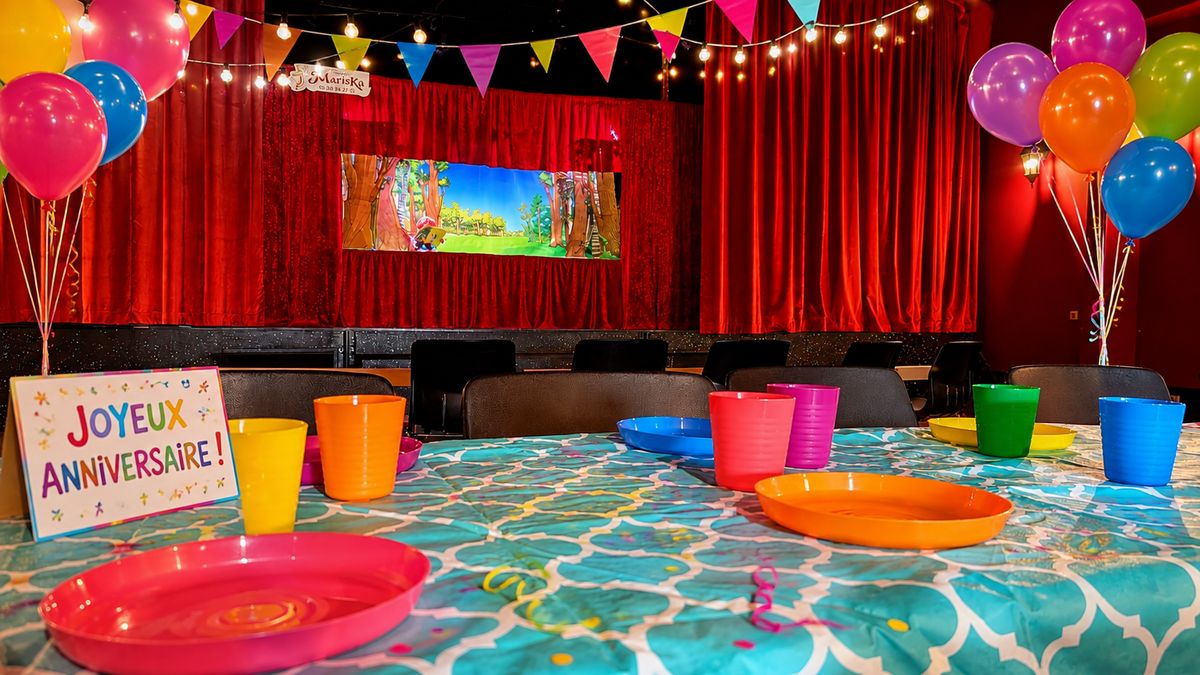 La salle de Lens préparée pour un anniversaire&nbsp;: table décorée, panneau « Joyeux anniversaire », ballons et guirlandes devant la scène au rideau rouge